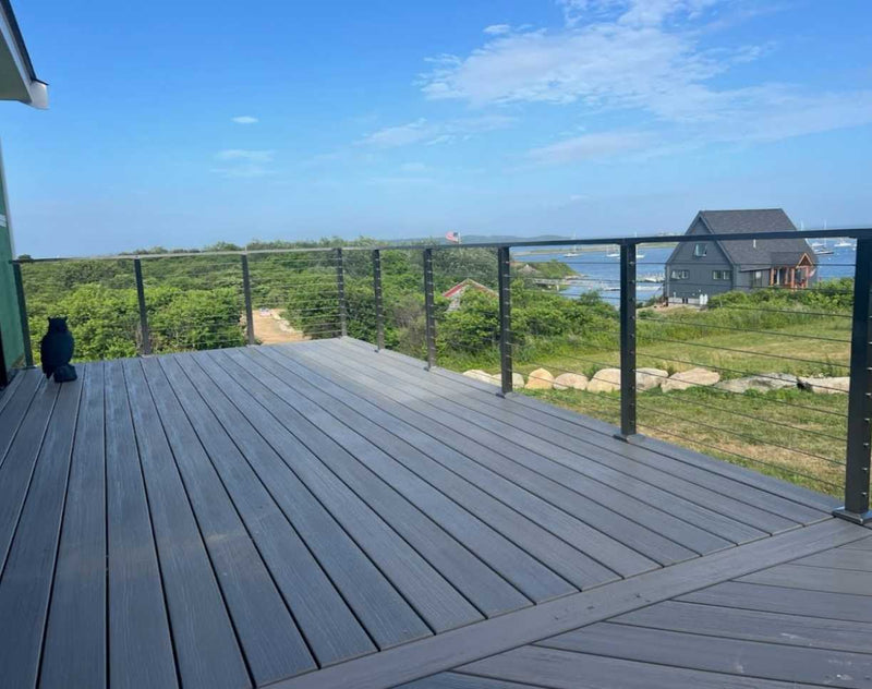 Gray deck with metal railing overlooking a scenic landscape with houses and greenery.
